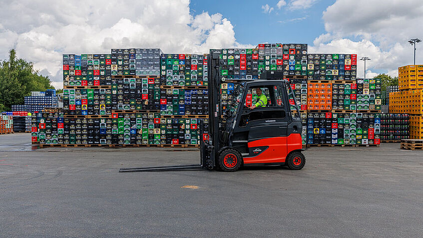 Ein roter Gabelstapler fährt übers das Gelände des Getränkelogistikers Essman in Wattenbek. Im Hintergrund stehen gestapelte Getränkekisten. 