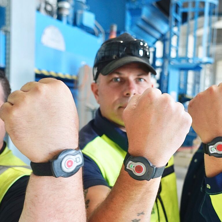 Drei Mitarbeiter von Smurfit Kappa Recycling halten ihre Transponderuhren am Handgelenkt ins Bild.