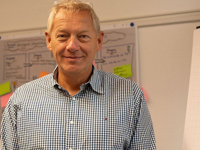  Henning Lankenau, ein Mann mit kurzen grauen Haaren steht neben einem Flipchart und blickt freundlich in die Kamera. 