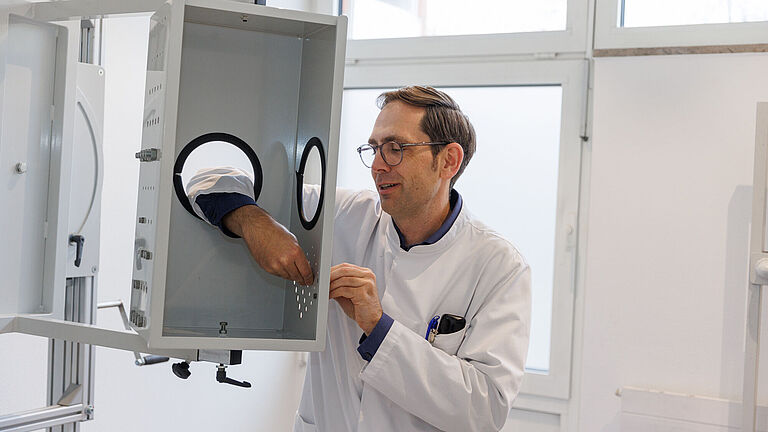Dr. Sven Jung,ehemaliger Leiter der Abteilung für BG Rehabilitation der BG Klinik Bergmannsheil Bochum, arbeitsplatzbezogene Therapieplatz. Er steht vor einer Metallrahmen und steckt die Hand durch, als würde er eine Schraube eindrehen. 