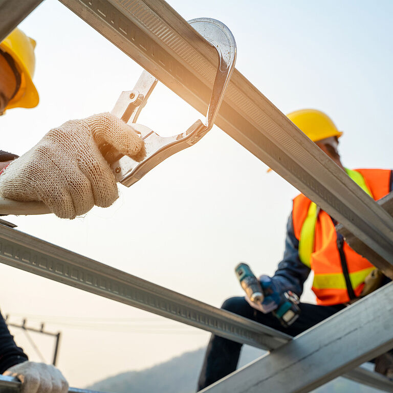 Zwei Männer mit Schutzkleidung und Helmen sind bei Arbeiten in der Höhe zu sehen.