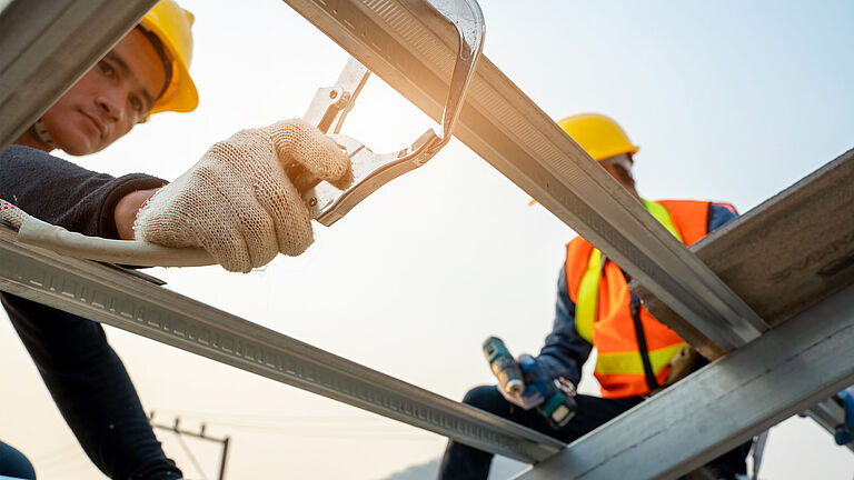 Zwei Männer mit Schutzkleidung und Helmen sind bei Arbeiten in der Höhe zu sehen.